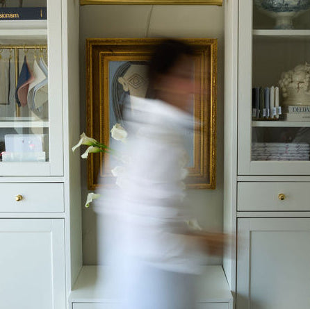 White glass-fronted cabinets with decorative items in a room with a blurred person in the foreground.