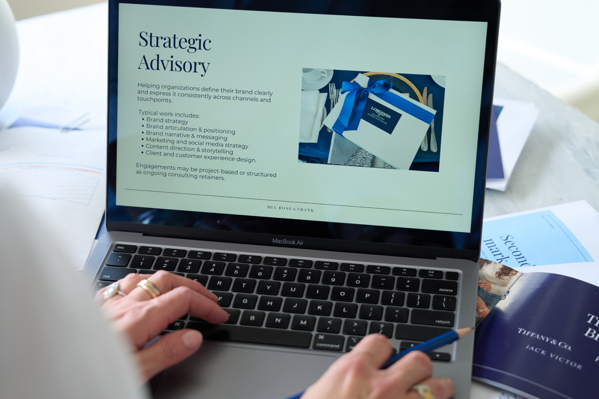 Person using a laptop with a screen displaying 'Strategic Advisory' on a desk with papers and a pen.